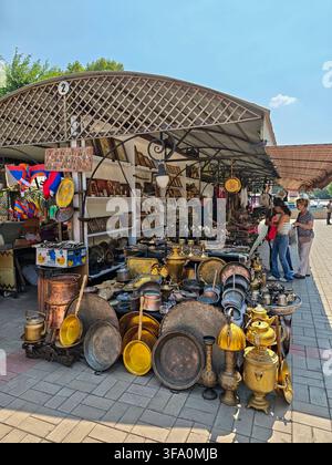 Market stall with copper and brass goods under a wooden canopy. Items include pots, pans, lanterns, and decorative pieces. People browse items on a pa Stock Photo