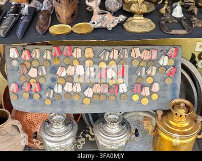 Vintage medal collection displayed on wooden board. Various medals with ribbons arranged in rows. Antique metal lanterns and decorative items surround Stock Photo