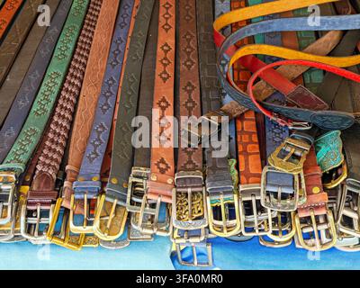 Collection of colorful belts with various patterns and metal buckles. Belts lie on blue surface, showcasing different textures and designs. Some belts Stock Photo
