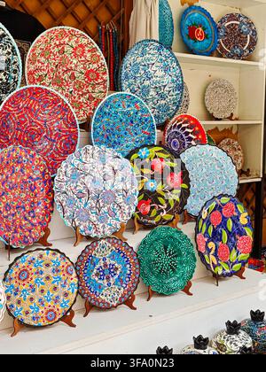 Vibrant, hand-painted ceramic plates displayed on wooden stands. Plates feature colorful floral and geometric patterns. Background shelves hold more d Stock Photo