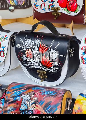 Hand-painted leather bag with floral embroidery and brass hardware. Colorful, artistic bags displayed in a shop setting. Vibrant red and white floral Stock Photo
