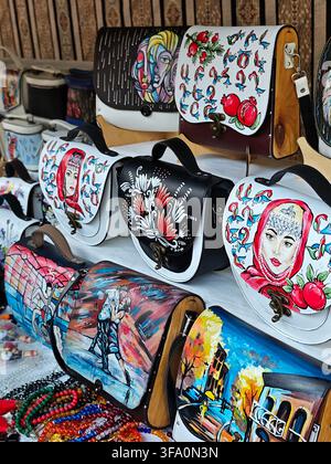 Hand-painted leather bags with colorful artistic designs. Each bag features unique, vibrant artwork. Bags are displayed on a wooden surface. Some show Stock Photo