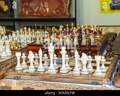 Chess sets arranged on wooden boards in shop display. White and dark pieces visible on checkered surfaces. Multiple sets showcase different materials Stock Photo