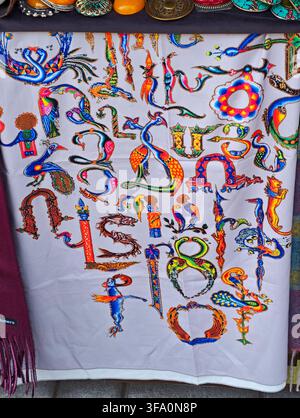 White textile displays colorful, stylized lettering and symbols. Vibrant threads form abstract patterns, including animal and geometric shapes. Textil Stock Photo