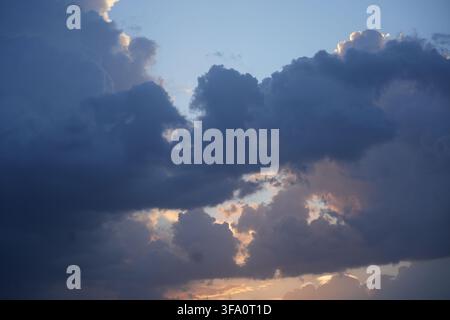Dramatic sunset glowing behind heavy dark storm clouds and blue sky Stock Photo