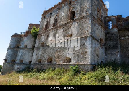 Weathered stone walls and multi story palace ruins of Medzhybizh fortress stand on grassy slope. Ancient fortification architecture features small emb Stock Photo
