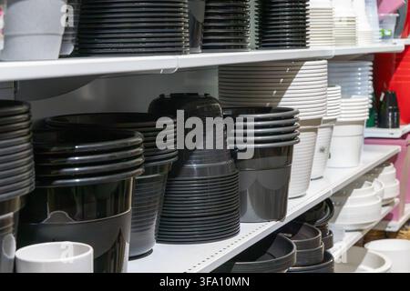 A variety of black and grey plastic containers for plants are displayed in rows on white shelving units Stock Photo