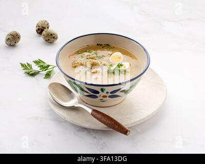 Clear chicken meatball soup served in a ceramic bowl with halved quail eggs, parsley, carrot, and a spoon on a white marble surface. Fresh quail eggs Stock Photo