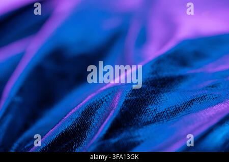 Close-up abstract textile surface with soft folds, illuminated by vivid blue and purple neon light. The detailed fabric texture creates a modern futur Stock Photo