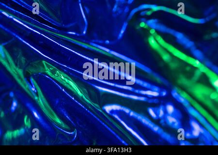 Macro abstract of crumpled iridescent foil with luminous blue and green reflections, creating a glossy futuristic texture background with flowing fold Stock Photo