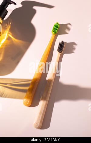 Bamboo toothbrushes beside a pump bottle on a sunlit pastel surface, casting bold shadows to illustrate sustainable dental care and a creative morning Stock Photo