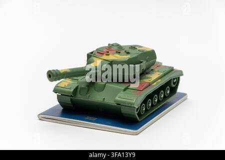 A green camouflage toy tank sits on a blue notebook against a white background. Stock Photo
