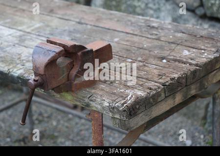 Rusty vise on a weathered wooden workbench outdoors, showing age, texture, and rugged industrial character. Stock Photo