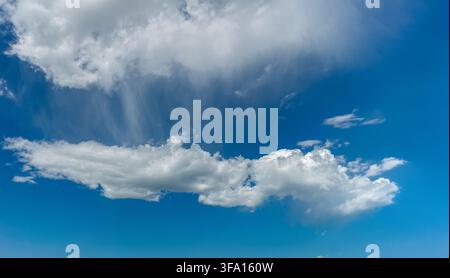 Scenic landscape view of white soft cumulus and wispy cirrus clouds floating in a bright vivid blue sky during daytime. Perfect for natural background Stock Photo
