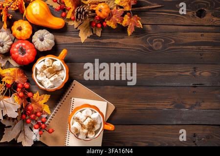 Autumn still life featuring two pumpkin shaped mugs filled with hot cocoa and marshmallows. Surrounded by decorative pumpkins. Fall leaves. And a note Stock Photo