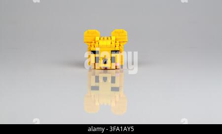 Cute yellow bear head figure made from miniature building blocks displayed on a reflective white surface. Stock Photo