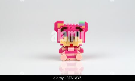 Cute pink bear figure made from miniature building blocks displayed on a reflective white surface against a neutral background. Stock Photo