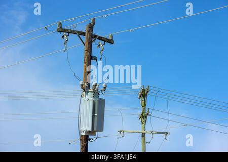 Electric poles hold power lines against bright blue sky poles support transformers cables. Stock Photo