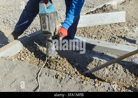 Worker is using jackhammer to break gravel at construction site Stock Photo