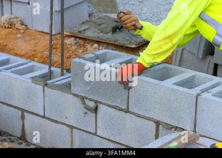 Masonry worker places concrete blocks carefully in row at construction site, build wall Stock Photo
