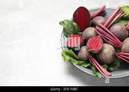 Whole and cut young beets with green leaves on gray textured table, closeup. Space for text Stock Photo