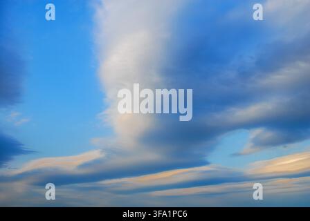 Scenic view of unique lenticular cloud formations and layered altocumulus structures glowing gently in a vibrant blue sky during dusk. Stock Photo