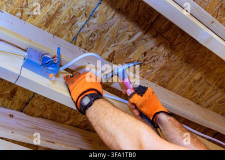 Electrical contractor is hammering wires to wooden beams while working on building project Stock Photo