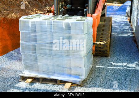 Worker uses machine to transport pallet of concrete blocks on gravel at construction site Stock Photo