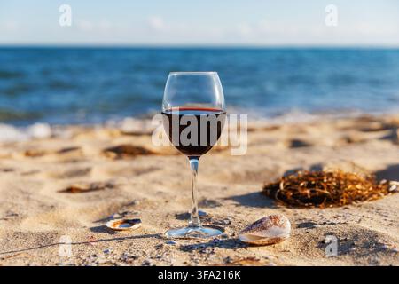 Coastal Wine Scene with Glass on Sand and Blue Sea Background Stock Photo