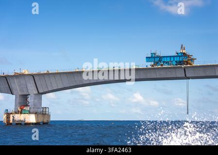 Heavy machinery and concrete pillars form a massive marine transportation bridge under construction across the tropical ocean in Maldives. Stock Photo