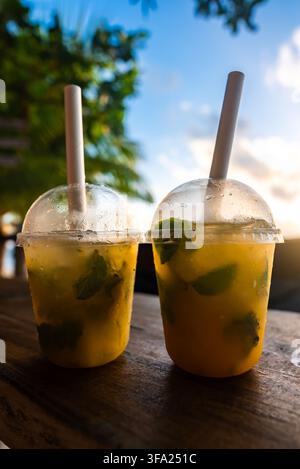 Two takeaway cups filled with chilled tropical drinks and paper straws rest on a rustic wooden table under a sunny sky in the Maldives. Stock Photo