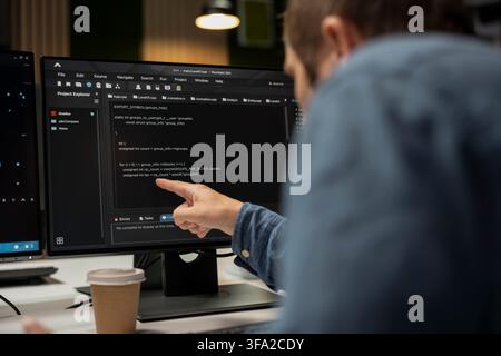 System administrator in startup office optimizing code for performance and scalability, doing quality assurance. IT worker following programming language written on PC screen with finger Stock Photo
