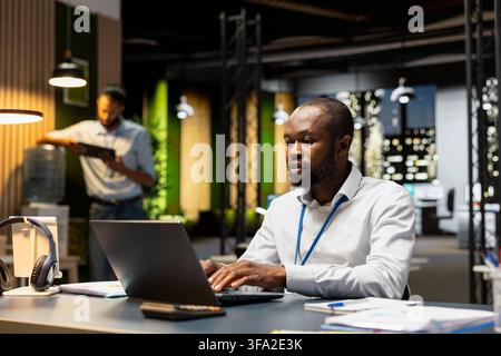 Employee completing spreadsheet on laptop, inputting and analyzing data. African american man typing on notebook keyboard, browsing internet, researching information online Stock Photo