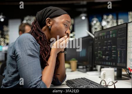 Tired programmer yawns at office desk while working late on computer for tech company. Exhausted software developer feeling fatigue while doing machine learning coding on PC Stock Photo