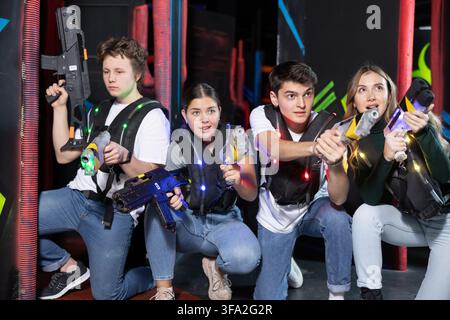 Four people having fun playing lasertag ducking behind cover in arena Stock Photo