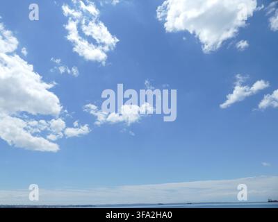 THESSALONIKI, GREECE - MAY 10, 2025 - White clouds are floating on a deep blue sky over a calm sea on a sunny day Stock Photo