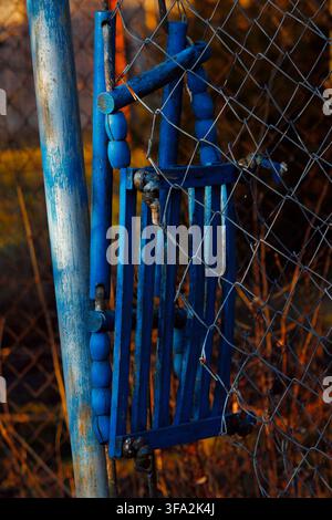 Abandoned royal blue wooden swing stuck on a worn frame in warm golden hour light with wire fence Stock Photo