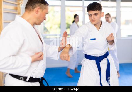 Young male attendee of karate classes fighting with middle-aged man in sports hall Stock Photo