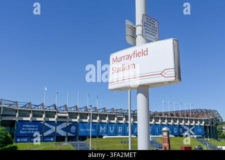 A sign to assist travellers for Murrayfield Edinburgh tram station with the iconic rugby and events stadium in the background under a clear blue sky. Stock Photo