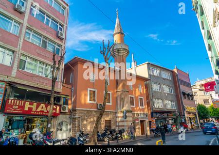 Istanbul, Turkey - 10 January, 2025: A vibrant orange mosque with a tall brick minaret is nestled between modern buildings and shops on a bustling cit Stock Photo