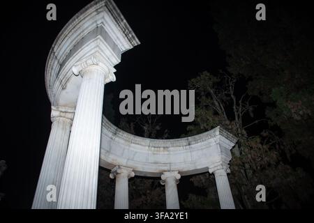 Dramatic upward view of a marble mausoleum rotunda featuring fluted Ionic columns and a curved cornice, lit against a black night sky. Stock Photo
