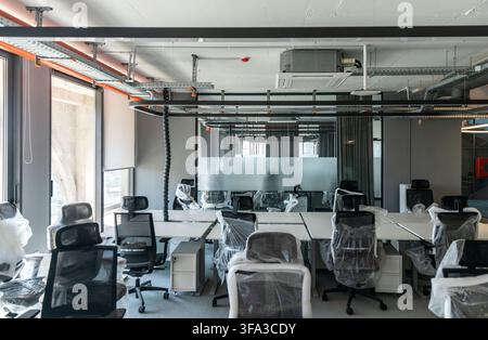 Empty open-plan office fitted with new desks, plastic-wrapped chairs and exposed ceiling cable trays ahead of its opening Stock Photo