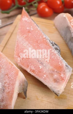 Fish pieces on a wooden board with cherry tomatoes nearby Stock Photo