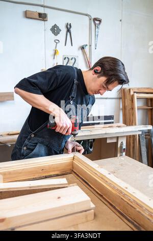 Focused woodworker finishing assembling vintage wooden window frame at workplace in workshop. Stock Photo