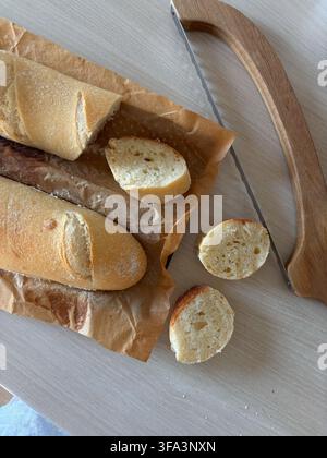 Sliced fresh baguette and kitchen knife on wooden cutting board, rustic breakfast or bakery concept. High quality photo Stock Photo