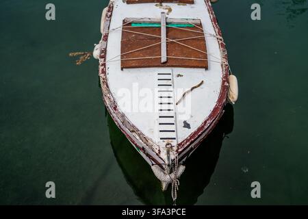 Overhead view of a weathered wooden boat floating on calm green water, showing its painted bow, deck and ropes. Suitable for travel, maritime and boat Stock Photo