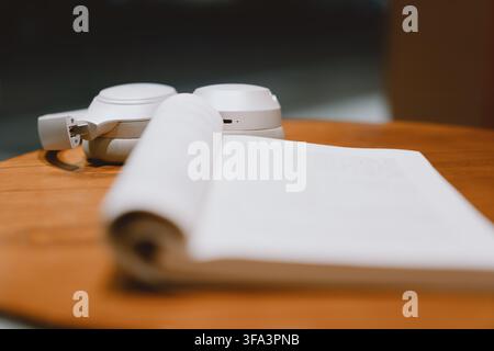 White wireless headphones and open notebook on wooden table in modern minimalist workspace — clean, Stock Photo