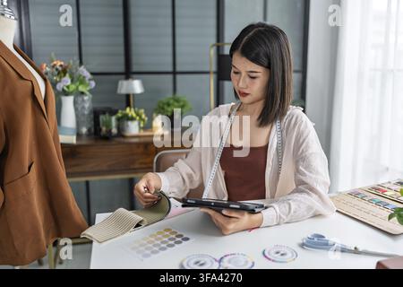 Asian woman fashion designer using tablet while working in creative fashion studio Stock Photo