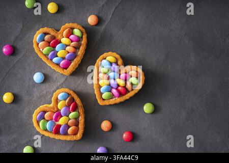 Colorful Candy Buttons on Heart shaped cake on black slate Background - Birthday concept Backgroundndy Buttons on Heart shaped cake on black slate Bac Stock Photo