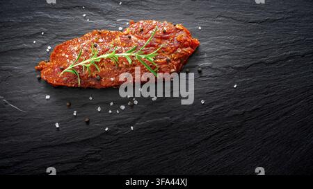 Raw marinated meat, beef steak on black slate background, top view Stock Photo